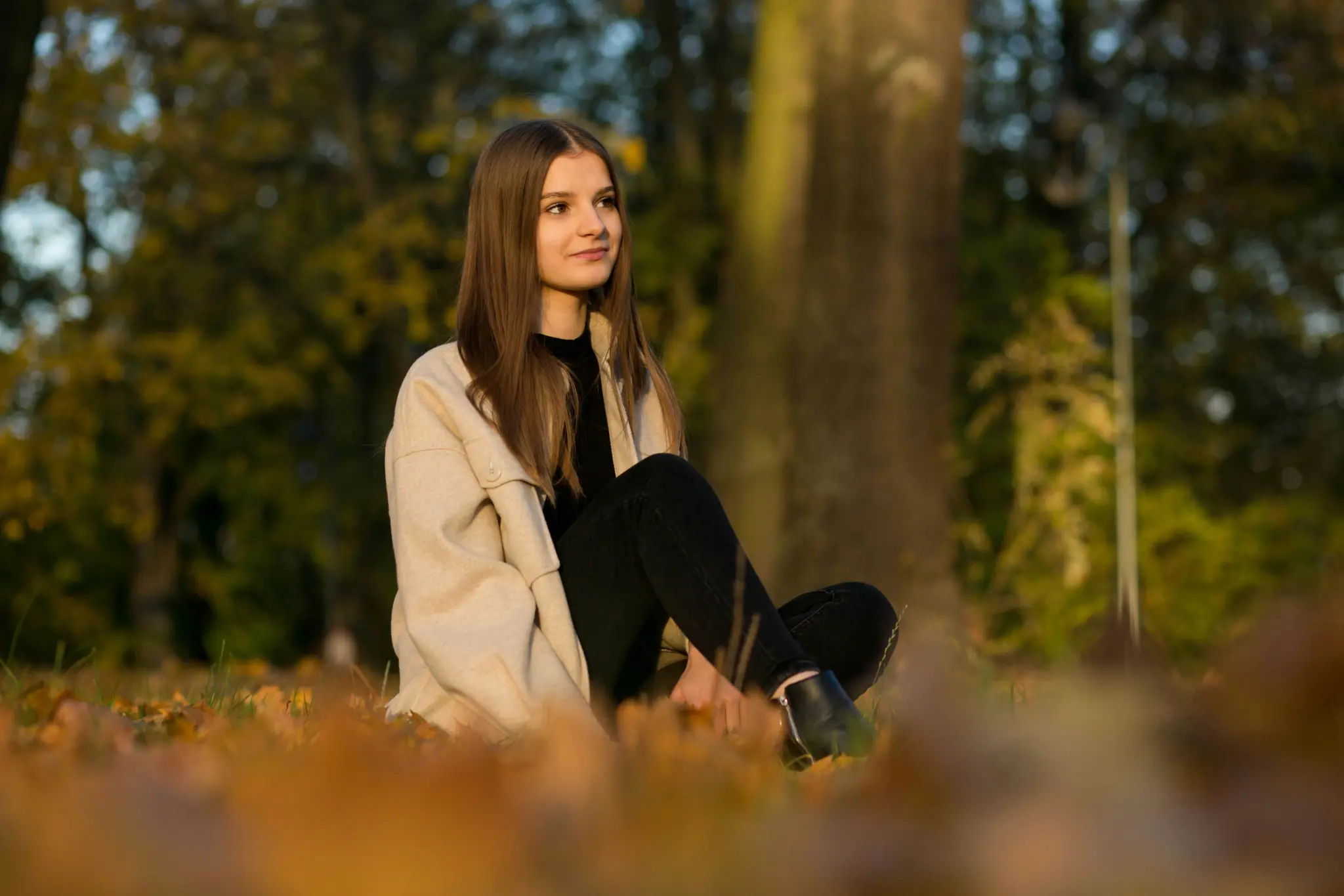 Ragazza adolescente seduta tra le foglie in un parco, assorta nei pensieri.